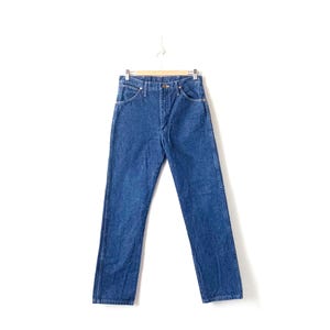May include: A pair of blue denim jeans hanging on a wooden hanger. The jeans have a classic straight leg style and a light wash.