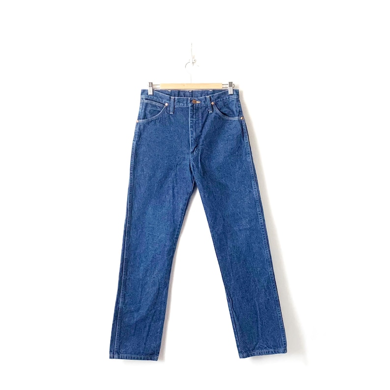 May include: A pair of blue denim jeans hanging on a wooden hanger. The jeans have a classic straight leg style and a light wash.