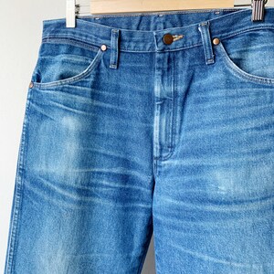 May include: A pair of blue denim jeans with a wooden hanger. The jeans have a classic five-pocket style and a straight leg.