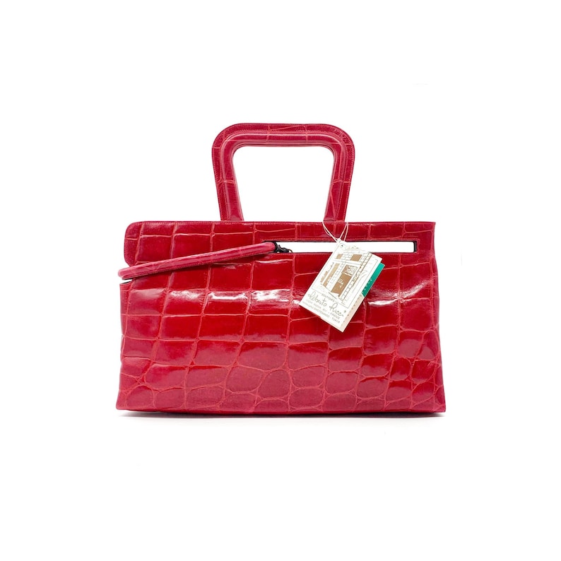 May include: A red crocodile embossed leather handbag with a unique top handle and a small tag that reads "Alberto Guardi"