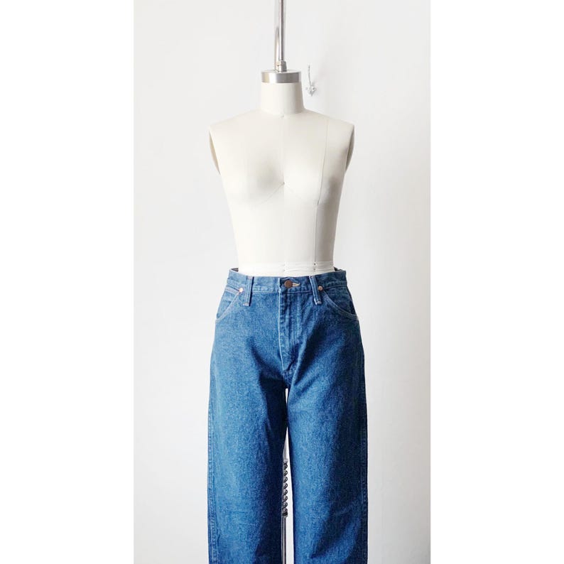 May include: A pair of blue denim jeans on a white dress form. The jeans have a high waist and a straight leg.