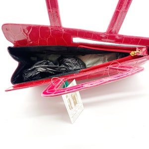 May include: A pink crocodile embossed leather handbag with a top handle and a detachable shoulder strap. The bag has a zipper closure and a gold-toned hardware.