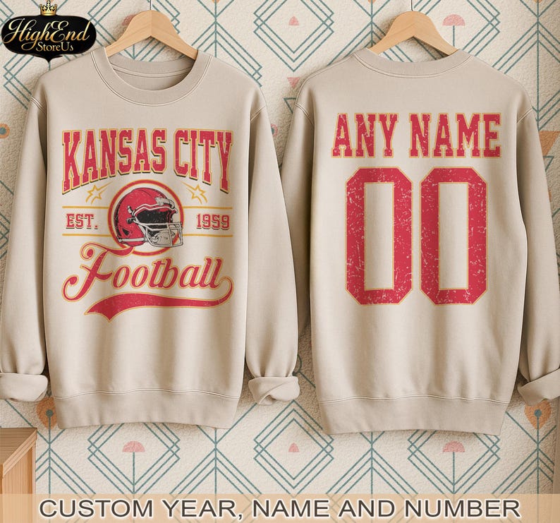 Puede incluir: Sudadera beige con un gr&aacute;fico de "Kansas City Football" en la parte delantera, con un casco de f&uacute;tbol americano rojo. La parte trasera muestra "ANY NAME" y el n&uacute;mero "00" en rojo. Opciones personalizadas de a&ntilde;o, nombre y n&uacute;mero.