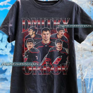 May include: Dark grey t-shirt with a vintage style graphic of a hockey player, with the name "Dmitry Orlov". The shirt includes the text "HighEndStoreUs". The design features a team of hockey players.