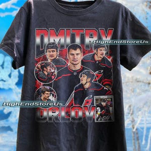 May include: Black t-shirt featuring a graphic of a hockey player with the name "Dmitry Orlov" in red and white lettering. The shirt includes multiple images of the player and the text "HighEndStoreUs".
