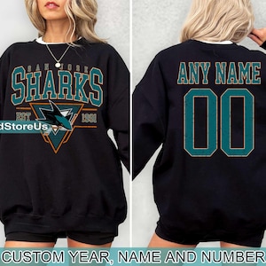 May include: Black sweatshirt with a teal San Jose Sharks logo and the text "San Jose Sharks Est 1991". The back of the sweatshirt has the text "Any Name 00" in teal.