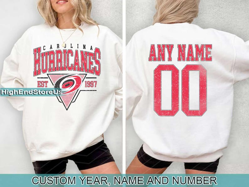 May include: White sweatshirt with a red and black Carolina Hurricanes logo and the text "Carolina Hurricanes Est 1997". The back of the sweatshirt has the text "Any Name" and a red number "00".