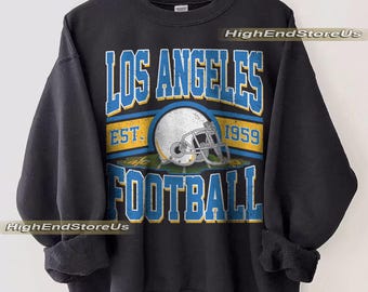 May include: Black sweatshirt featuring the text "LOS ANGELES FOOTBALL" in blue and white. A football helmet graphic is centered below the text. The sweatshirt also includes the text "EST. 1959".