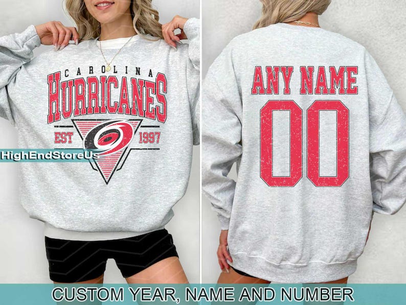 May include: A grey sweatshirt with a Carolina Hurricanes logo and the text "Carolina Hurricanes Est 1997". The back of the sweatshirt has the text "Any Name 00".