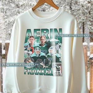 Puede incluir: Sudadera color crema con un dise&ntilde;o gr&aacute;fico verde y blanco con el nombre "AERIN FRANKEL". El dise&ntilde;o incluye im&aacute;genes de jugadores de hockey con uniformes verdes y blancos. El texto "HighEndStoreUs" tambi&eacute;n es visible.