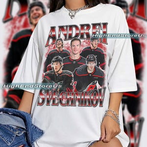 May include: White t-shirt featuring a vintage-style graphic of hockey player Andrei Svechnikov. The design includes the player's name and images of him and other players in black and red uniforms. The text "HighEndStoreUs" is also visible.