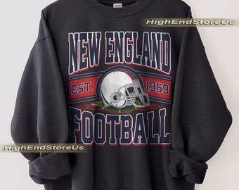 Könnte beinhalten: Schwarzes Sweatshirt mit dem Text "NEW ENGLAND FOOTBALL" in Weiß und Rot, mit einer Footballhelm-Grafik. Der Text "EST. 1959" ist ebenfalls enthalten. Das Sweatshirt hängt an einem Holzkleiderbügel.