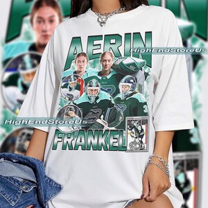 Puede incluir: Camiseta blanca con un dise&ntilde;o gr&aacute;fico verde y blanco. El dise&ntilde;o presenta el nombre "AERIN FRANKEL" e im&aacute;genes de una jugadora de hockey sobre hielo en verde azulado y verde. El texto "HighEndStoreUs" tambi&eacute;n es visible.