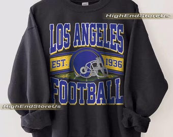 May include: Black sweatshirt featuring the text "LOS ANGELES FOOTBALL" in blue and white. A blue football helmet is centered on the shirt, with the year "1936" above it. The words "HighEndStoreUs" are printed on the shirt.