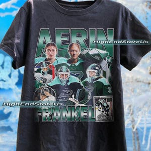 May include: Dark grey t-shirt with a hockey-themed design. It features images of a hockey player and the name "AERIN FRANKEL" in green and white. The text "HighEndStoreUs" is also visible. The design includes a hockey card.