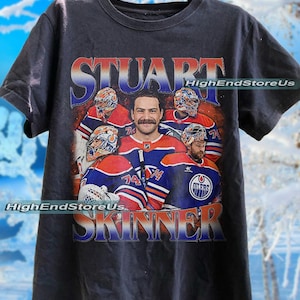 May include: Black t-shirt featuring a graphic of Stuart Skinner, an ice hockey player, with the text "STUART SKINNER" in a vintage style. The design includes images of Skinner and his team's logo. The text "HighEndStoreUs" is also visible.