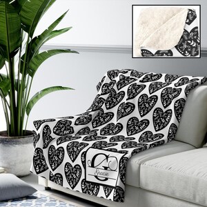 May include: A white throw blanket with a black heart pattern, draped over a white sofa. The blanket features a personalized monogram with the name "Gracie". The reverse side of the blanket is a soft, cream-coloured material.