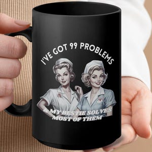 May include: Black coffee mug with a white graphic of two women in nurse uniforms. The text reads "I've got 99 problems and my bestie solves most of them."