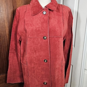 May include: A red suede jacket with a collared neckline and three button closure. The jacket has long sleeves and a tailored fit. The jacket is displayed on a mannequin. The jacket is approximately 30 inches long.