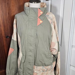 Peut inclure: Veste vert olive avec des imprimés de cartes. La veste a un col montant, des accents pêche et des boutons dorés. Les manches et le bas de la veste présentent une impression de carte vintage.