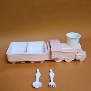 Puede incluir: Una bandeja de comida rosa de plástico con forma de Chow Chow Train con una taza, cuchara y tenedor blancos. La bandeja tiene dos compartimentos y las palabras "CHOW CHOW TRAIN" impresas en el lateral.