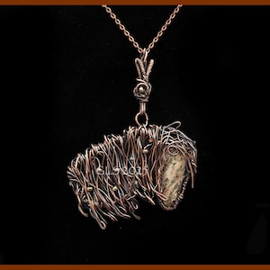 Pode incluir: Um colar com pingente artesanal de arame de cobre com um design de bisonte. O pingente incorpora uma pedra natural e é suspenso por uma corrente delicada. O bisonte é intrincadamente tecido com arame de cobre, mostrando um estilo artístico único.