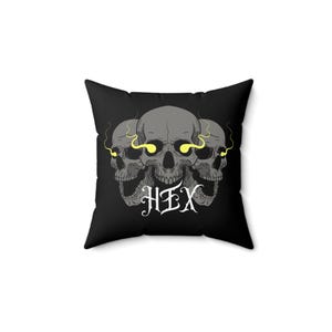 May include: Black square throw pillow featuring a graphic of three gray skulls with yellow glowing eyes and smoke. The word "HEX" is written in white gothic lettering below the skulls. The pillow is a decorative item.