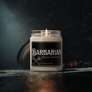 May include: A beige soy candle in a glass jar with a black label that reads "Barbarian Smells... Reckless."  The label also features a graphic of two crossed axes.