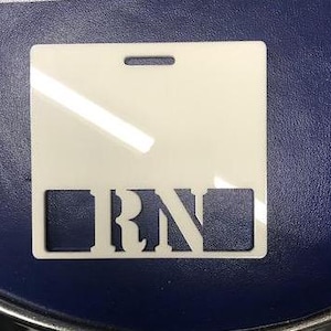 May include: White plastic badge holder with a cut-out for a name tag and the letters "RN" in a stylised font.