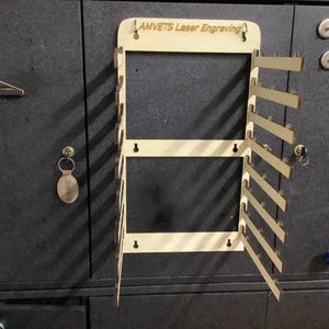 Pode incluir: Um suporte de parede de madeira com o texto "AMVETS Laser Engraving" no topo. O suporte tem várias ranhuras para guardar itens, como chaves ou joias.