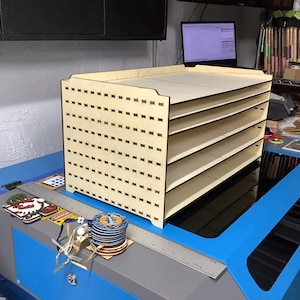 May include: A wooden shelf unit with five shelves, each with a grid pattern. The shelf unit is made of light wood and has a natural finish. The shelf unit is sitting on a blue surface.