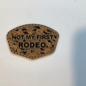 May include: A wooden cutout with a floral design and the text "NOT MY FIRST RODEO" in black.