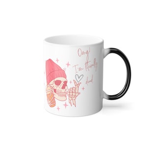 Puede incluir: Taza de café de cerámica blanca con asa negra. La taza tiene una ilustración rosa y blanca de una calavera con un gorro rosa y sosteniendo una bebida. El texto "Omg! I'm literally dead" está escrito en rosa en la taza.
