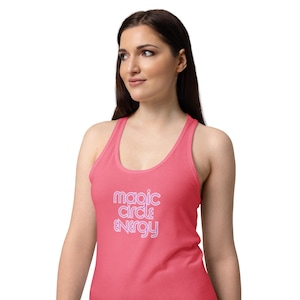 Könnte beinhalten: Ein korallenfarbenes Tanktop mit den Worten "magic circle & energy" in hellvioletter Schrift. Das Oberteil hat ein Racerback-Design und ist aus einem weichen Material gefertigt. Das Tanktop ist ein Freizeitkleidungsstück.