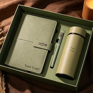 May include: A green gift set containing a notebook, pen, and flask, presented in a green box. The notebook has a tab closure and the text "Your Logo". The flask also has the text "Your Logo". A lit candle is placed nearby.