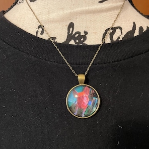 May include: A gold chain necklace with a round glass pendant featuring a colorful image of a dog.