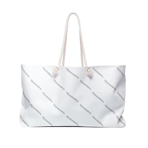 May include: White canvas tote bag with a repeating pattern of grey swords. The bag has white rope handles with gold metal accents.