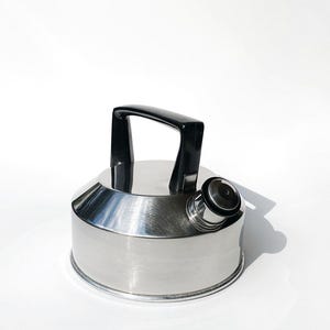 Könnte beinhalten: Ein silberner Wasserkocher mit schwarzem Griff und Ausguss. Der Wasserkocher hat eine glänzende, polierte Oberfläche.