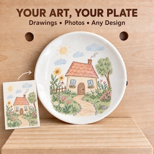 Pode incluir: Um prato de cerâmica branca com uma ilustração colorida de uma casa com telhado vermelho, um caminho de pedra, girassóis e uma árvore. O texto "YOUR ART, YOUR PLATE Drawings • Photos • Any Design" está impresso acima do prato.