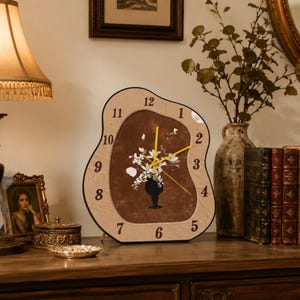 Puede incluir: Un reloj de pared de madera con una forma orgánica única. La esfera del reloj presenta un centro marrón con un arreglo floral en un jarrón negro. Las manecillas del reloj son amarillas y los números están en una fuente clásica.