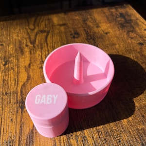 May include: Pink plastic ring holder with a small pink container labelled "GABY".