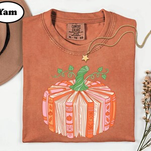a brown t-shirt with a pumpkin graphic and a necklace, along with a hat and some flowers, all arranged on a white background.