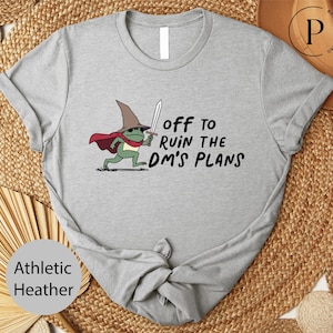 A gray t-shirt with a cartoon frog wearing a wizard's hat and holding a sword, along with the text "Off to ruin the dm's plans".