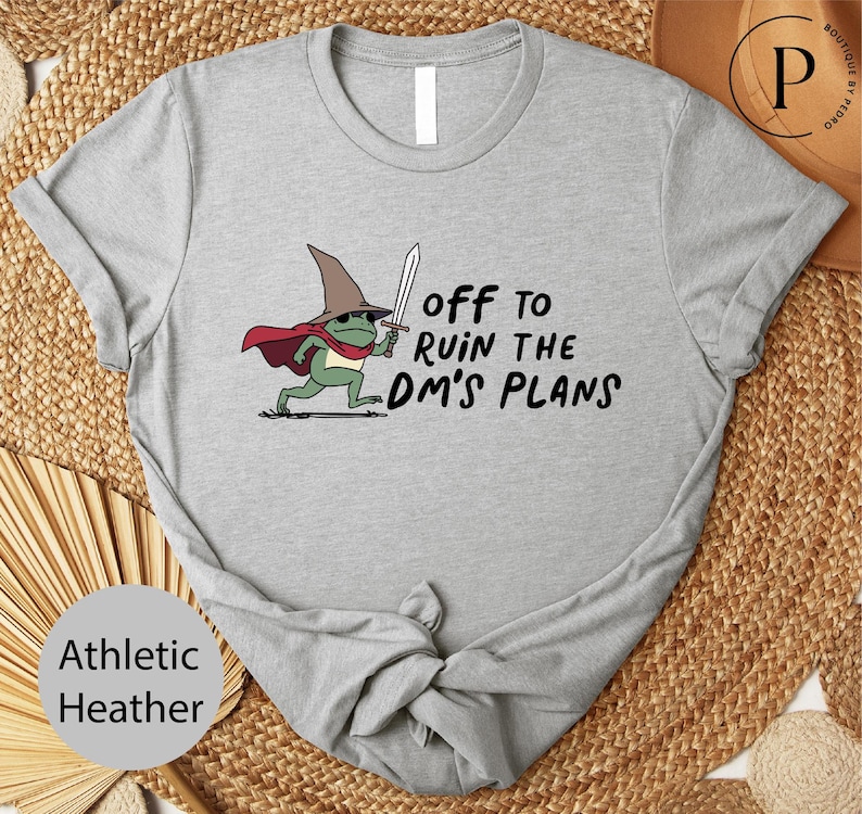A gray t-shirt with a cartoon frog wearing a wizard's hat and holding a sword, along with the text "Off to ruin the dm's plans".