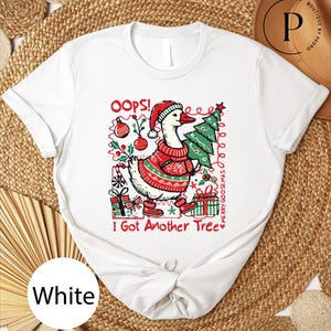 May include: White t-shirt featuring a cartoon goose wearing a Santa hat and sweater, carrying a Christmas tree. The text "OOPS! I Got Another Tree" and "Merry Goose Mas" are also visible. The design includes Christmas ornaments and gift boxes.