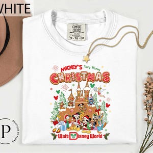 A white t-shirt with a colorful graphic design depicting Disney characters and a castle, along with the text " Mickey's Very Merry Christmas Walt Disney World".