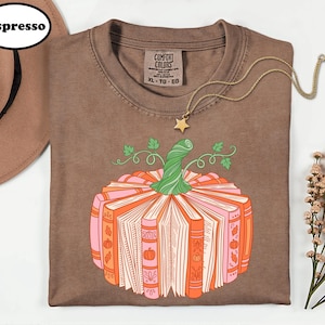 a brown t-shirt with a pumpkin graphic and a necklace, along with a hat and some flowers, all arranged on a white background.