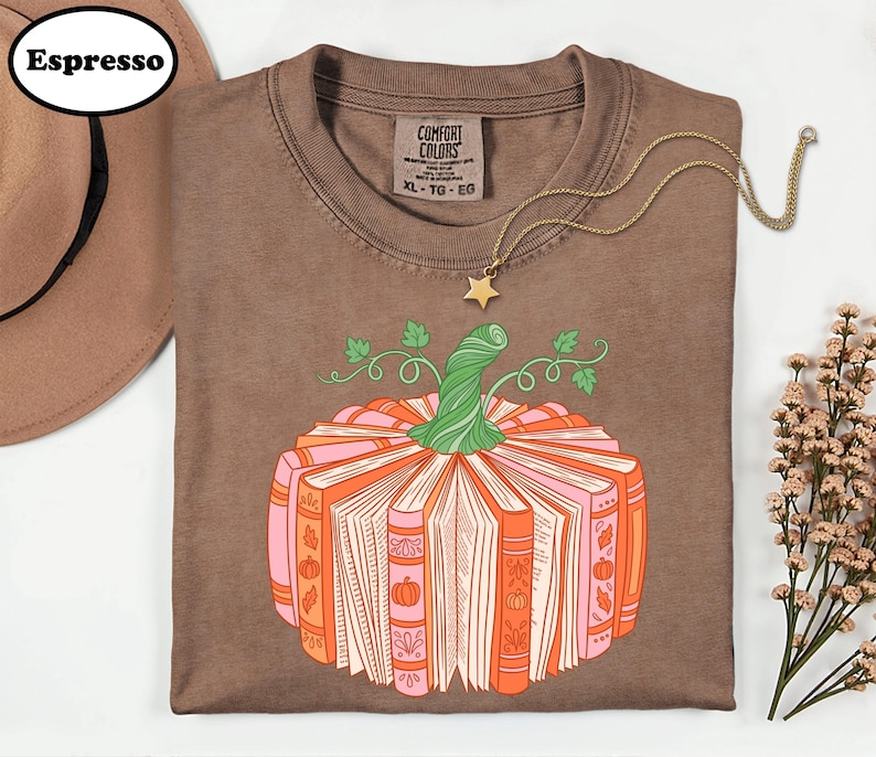 a brown t-shirt with a pumpkin graphic and a necklace, along with a hat and some flowers, all arranged on a white background.