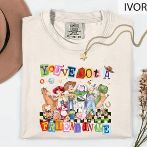 A white t-shirt with a colorful graphic design featuring characters from the Toy Story movie, along with the text "You've Got a Friend in Me".