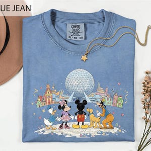 A blue t-shirt with a graphic of Disney characters Mickey Mouse, Minnie Mouse, Donald Duck, and Goofy, along with a large globe, is displayed on a white surface.